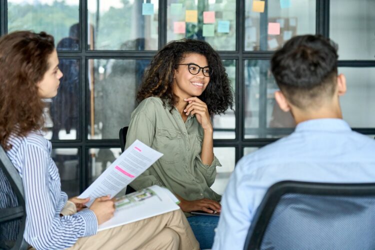 Diverse smiling happy colleagues listening to mentor leader in modern office.