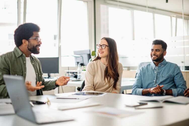 A spirited discussion unfolds in a light-filled office, where a man in a green shirt gestures animatedly