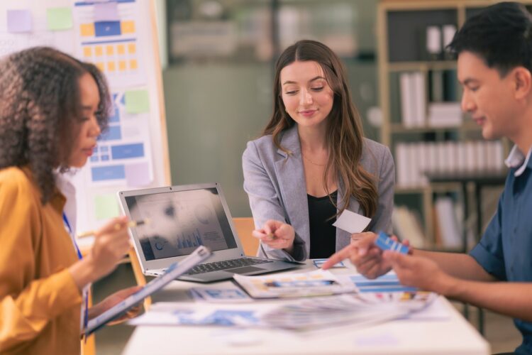 A team of UI UX web designers are working together to develop a mobile responsive website while discussing a project at a modern conference table. Brainstorming